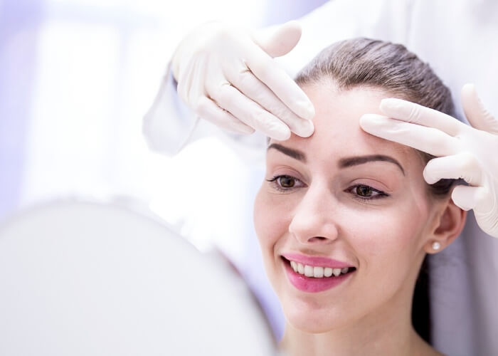 A doctor touches a young woman's forehead as she looks in a mirror