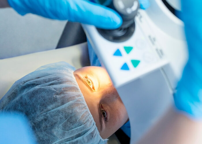 Young woman wearing a surgical hair cover while laying beneath an optical laser machine